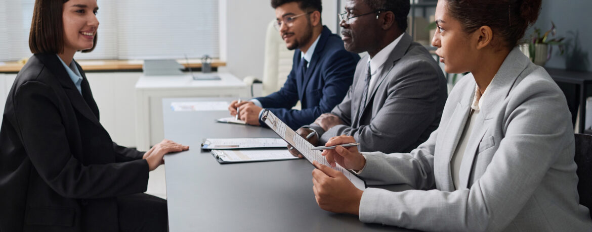 Professional woman interviewing for an office job with a panel of three interviewers.