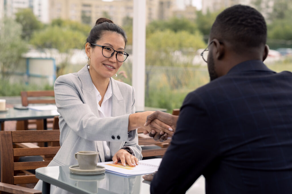 Happy young businesswoman shaking hand of business partner over table after negotiating job offer.